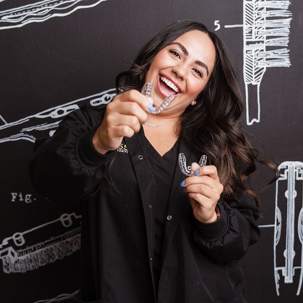 A woman is holding aligners and smiling