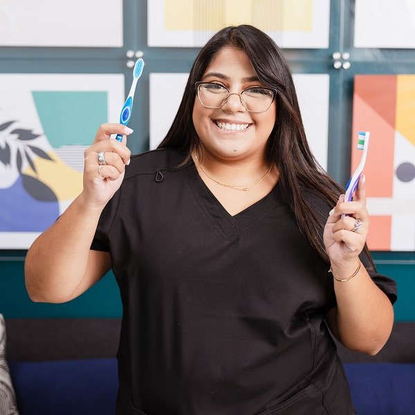 A woman is joyfully smiling with two toothbrushes in her hands