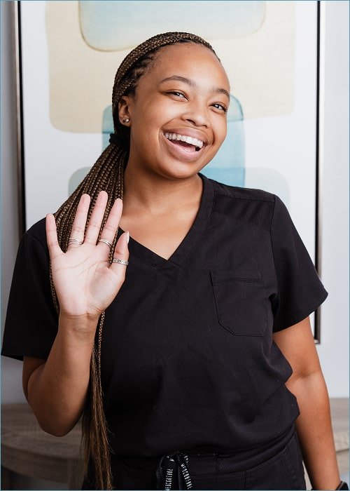 A woman is smiling and waving to the camera