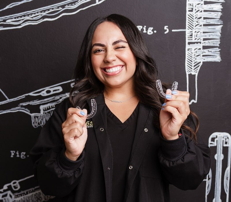 A woman is smiling with clear aligners in her hands