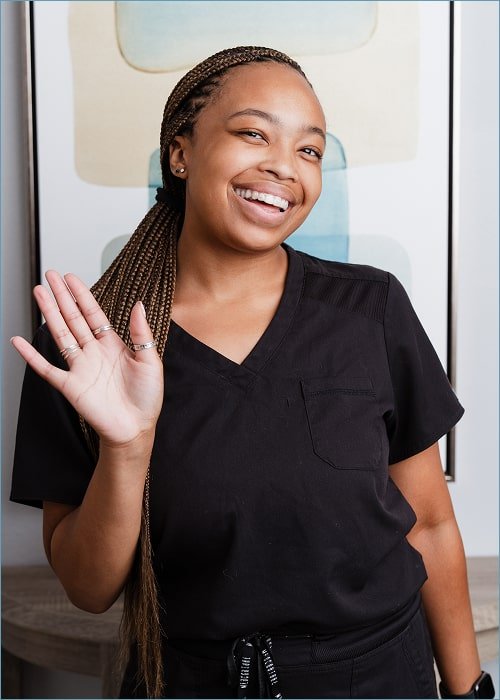 A woman is waving hello and joyfully smiling at brush365 dental office