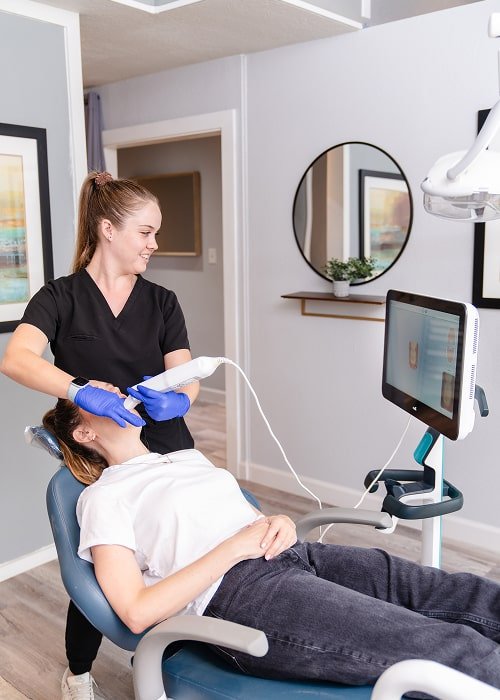 Top dentist smiling while performing 3d scan procedure to joyful patient in a dental chair